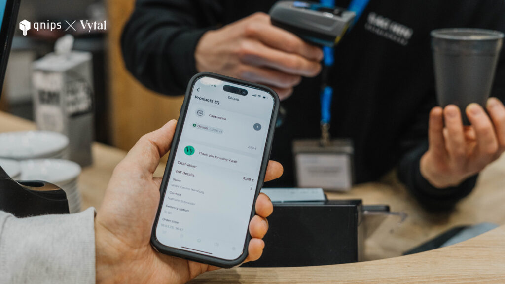 A person is holding a smartphone on which the shopping basket of the qnips app is open and the Vytal button is visible. 