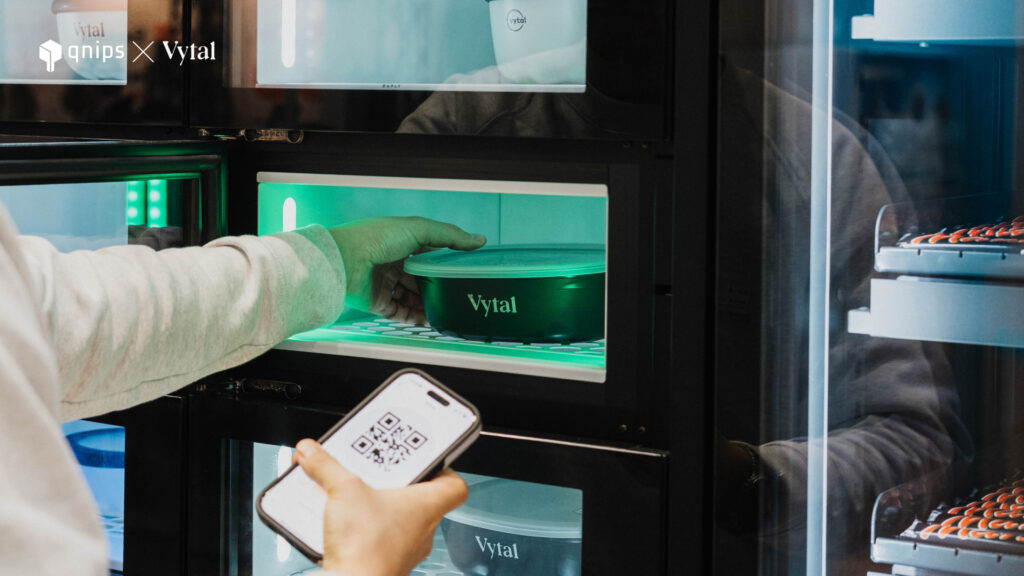 One person takes a Vytal reusable bowl from the pick-up box and holds a smartphone with a QR code on it in the other hand. 