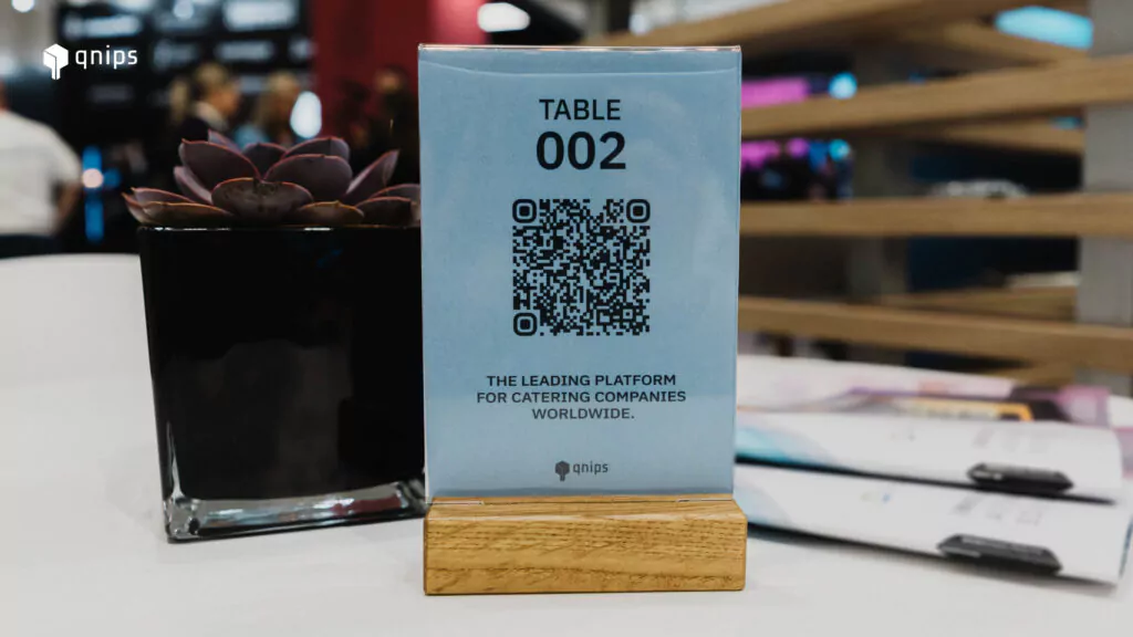 Das Bild zeigt einen Aufsteller, der auf einem Tisch platziert ist. Auf dem Aufsteller ist ein QR Code zu sehen, der für den Tischservice gescannt werden kann.
