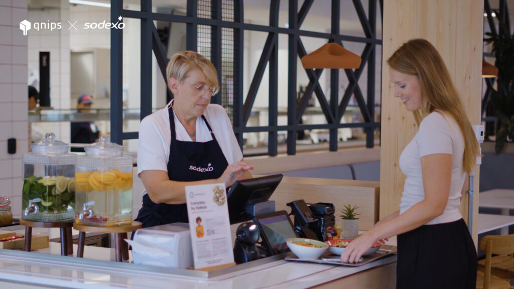 The picture shows a kitchen assistant taking payment from a woman at the cash register.